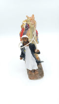 Bedouin man in a white robe and black coat leading a decorated pack camel holding a rope