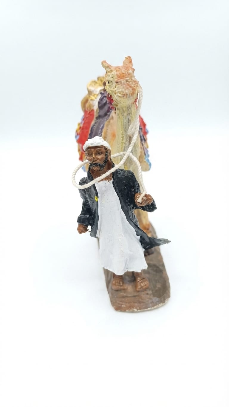 Bedouin man in a white robe and black coat leading a decorated pack camel holding a rope