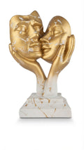 Two golden intertwined faces sculpture depicting two abstract faces kissed and cradled by hands on a white-and-gold marbled base