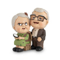 Charming elderly couple figurine of an older man standing next to an elderly woman seated on a chair while holding a magnifying glass